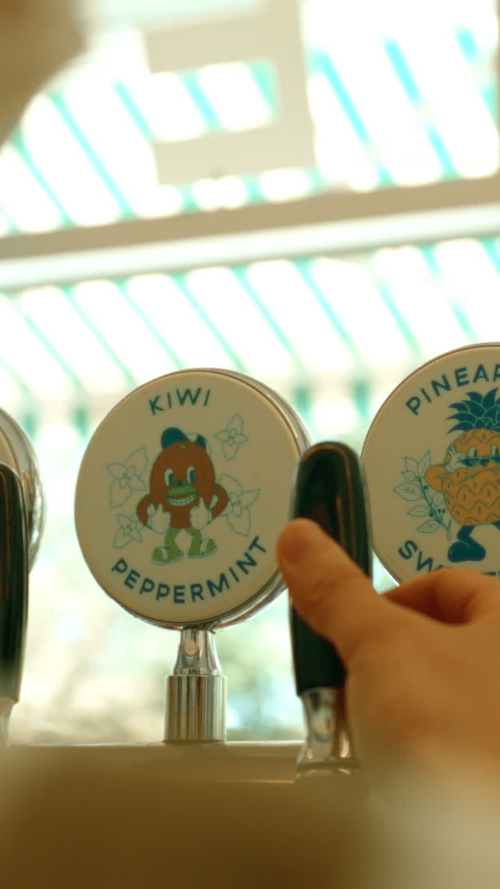 창가 카운터에 붙은 키위·파인애플 그림의 음료 탭과 그 손잡이를 잡은 손